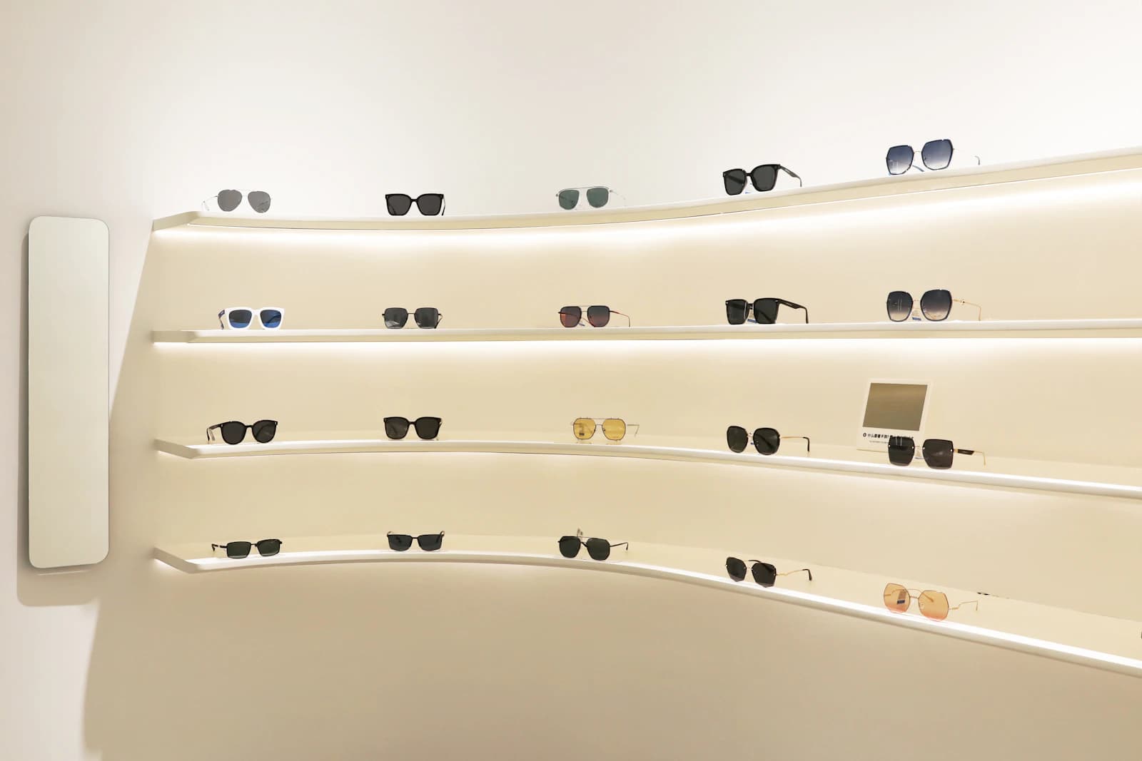 Backlit curved display shelves holding rows of luxury sunglasses in acetate and metal frames with grey, green and gradient lenses