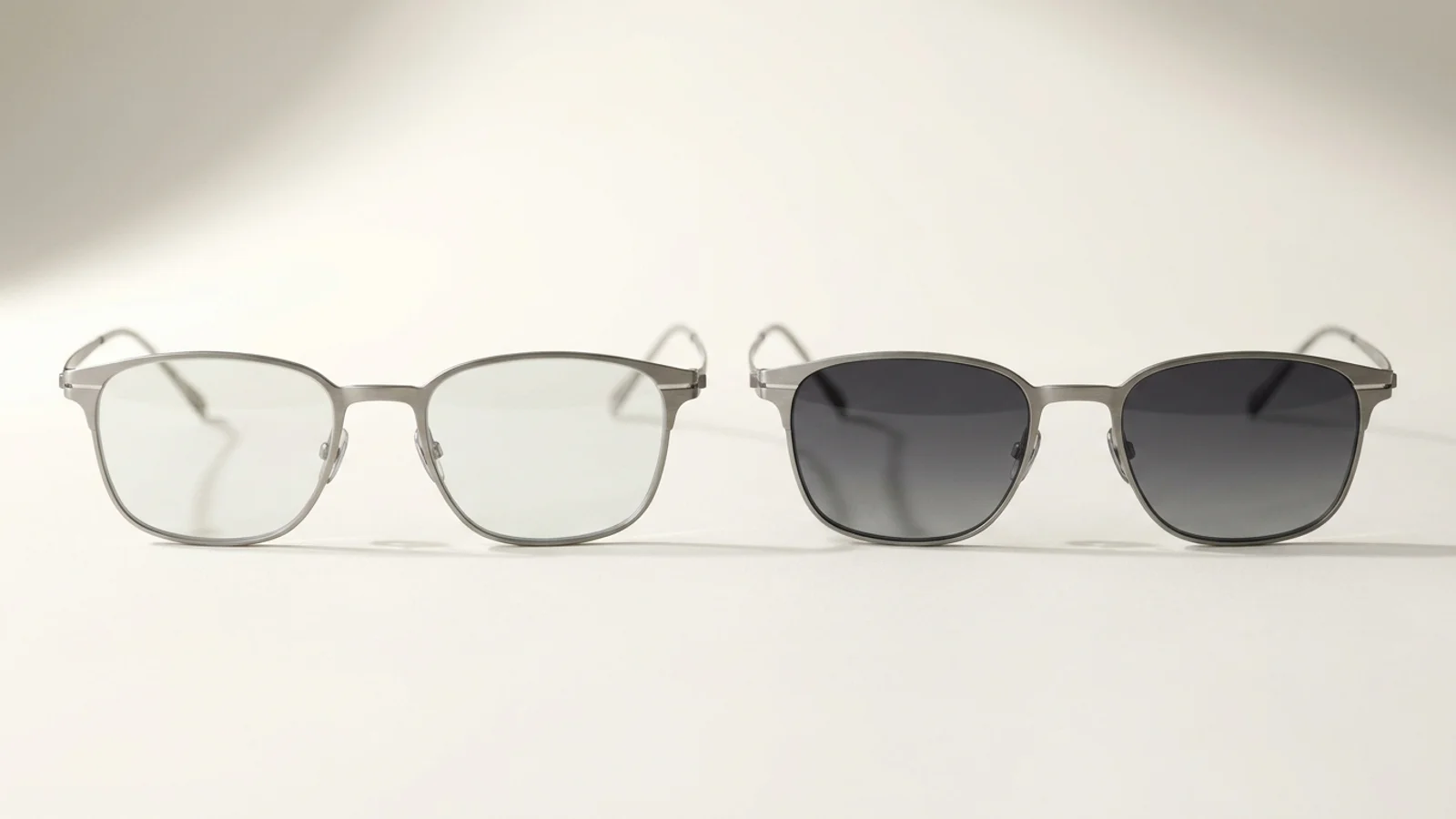Two pairs of photochromic glasses side by side, one darkened in sunlight and one nearly clear